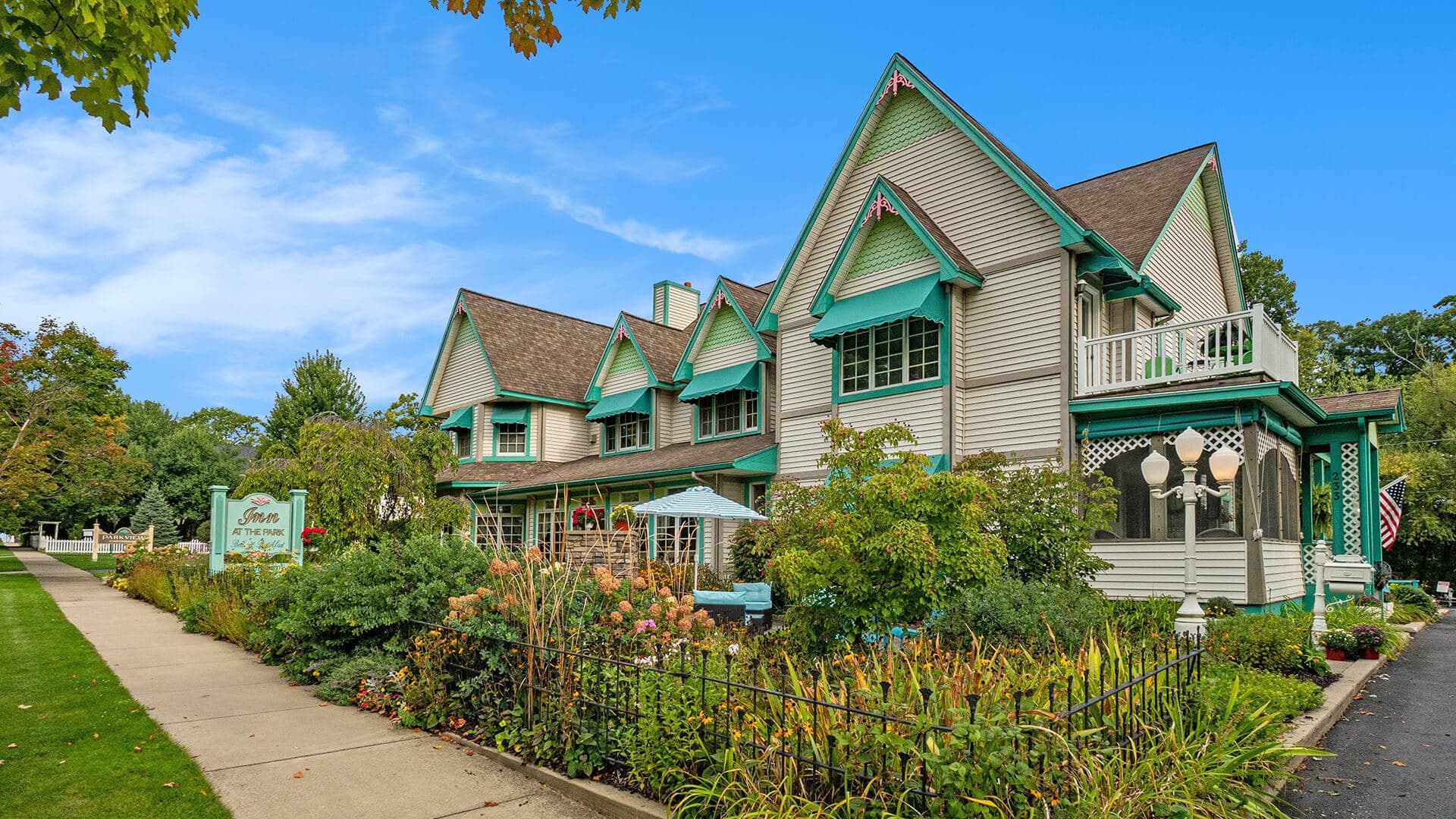 A charming two-story house with teal accent details surrounded by lush gardens.