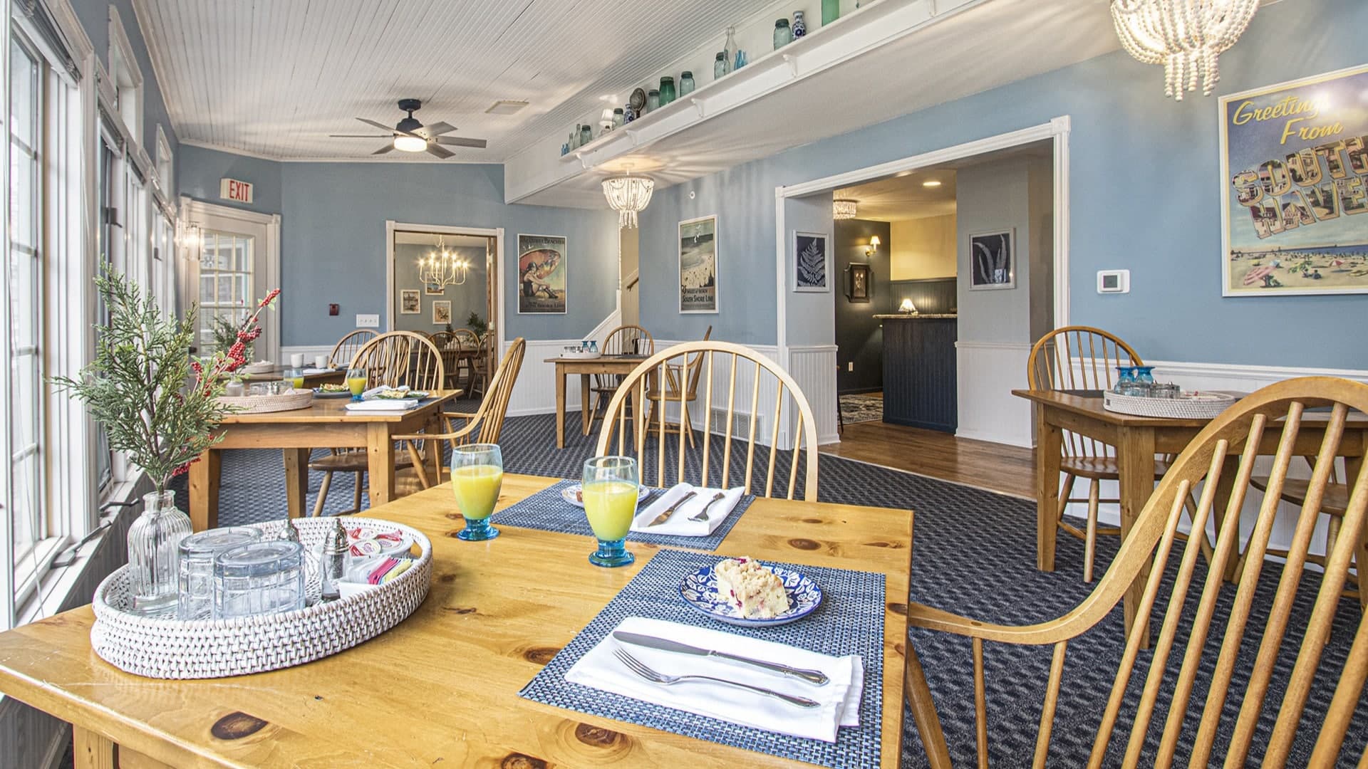 A bright dining area with wooden tables, blue walls, and natural light, featuring glasses of orange juice and dessert on the tables.