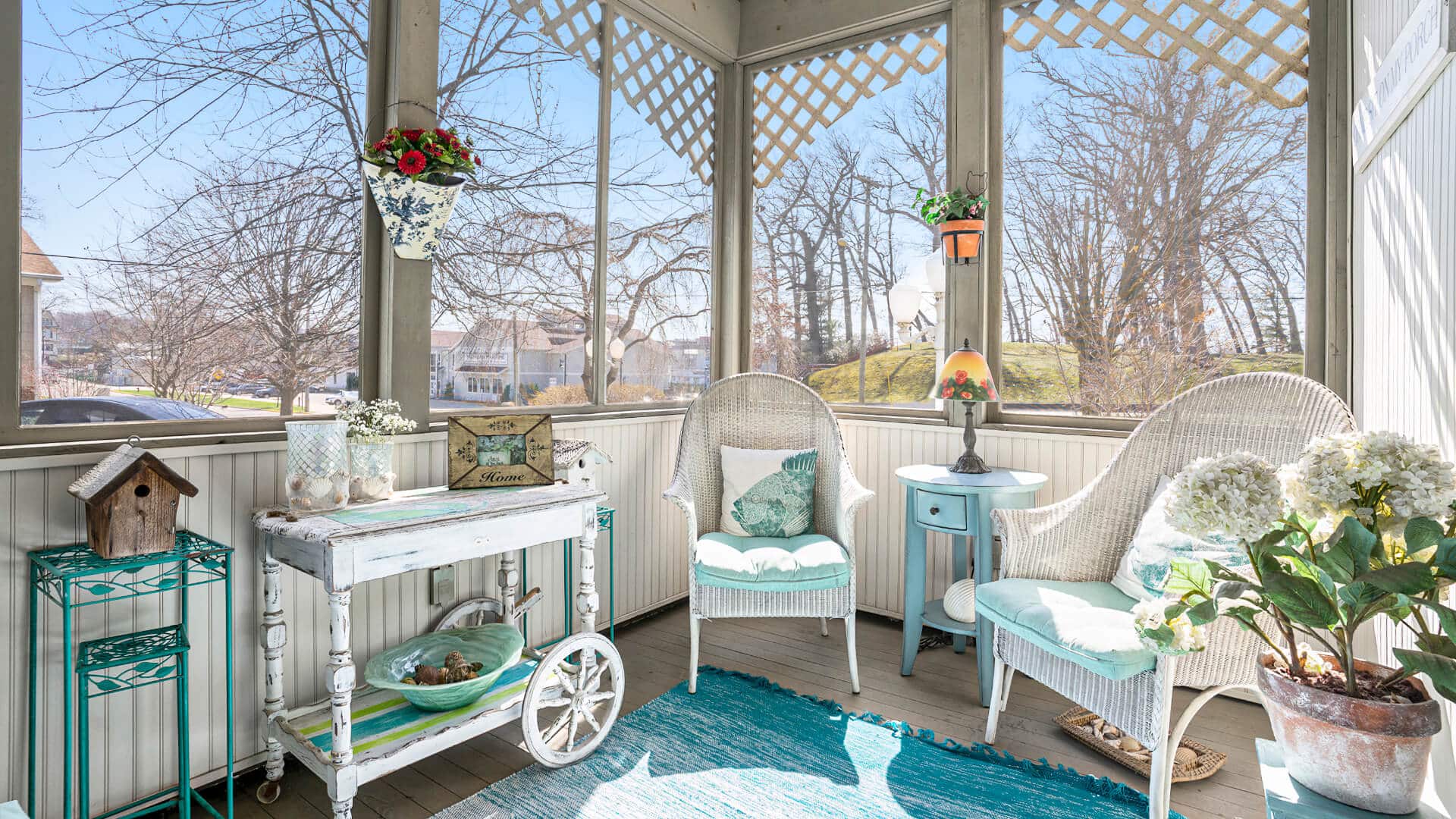 A cozy sunroom featuring two wicker chairs, a decorative table, and potted plants with a view of trees outside.