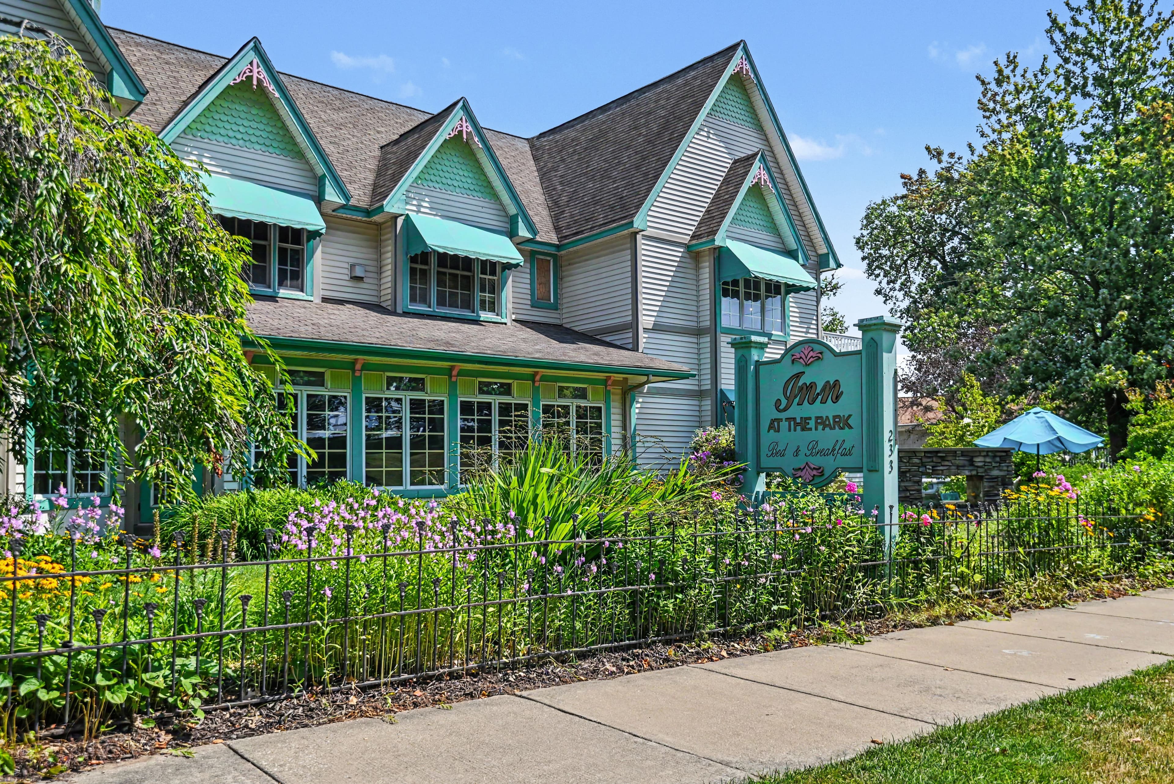 A charming, colorful inn surrounded by lush greenery and flowers, featuring a sign that reads "Inn at the Park."