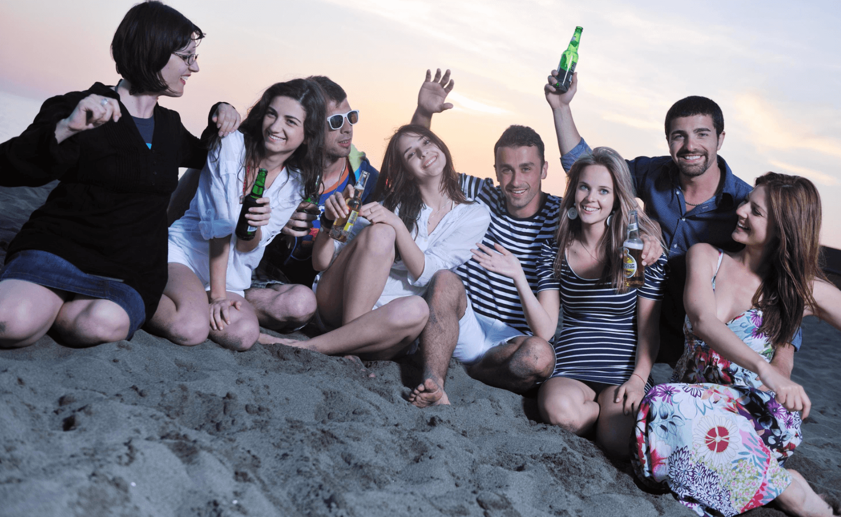 A group of eight friends poses on the beach at sunset, holding bottles and enjoying their time together. A group of eight friends poses on the beach at sunset, holding bottles and enjoying their time together.