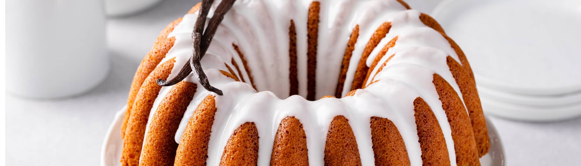 A round bundt cake drizzled with white icing and topped with a vanilla pod.