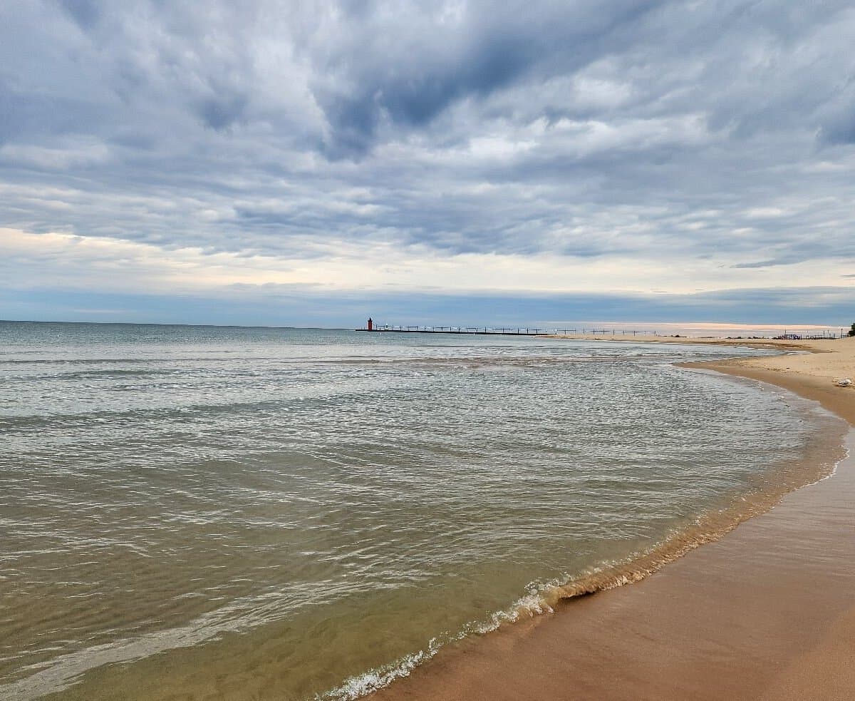 A tranquil beach scene with gentle waves under a cloudy sky and a distant lighthouse. A tranquil beach scene with gentle waves under a cloudy sky and a distant lighthouse.