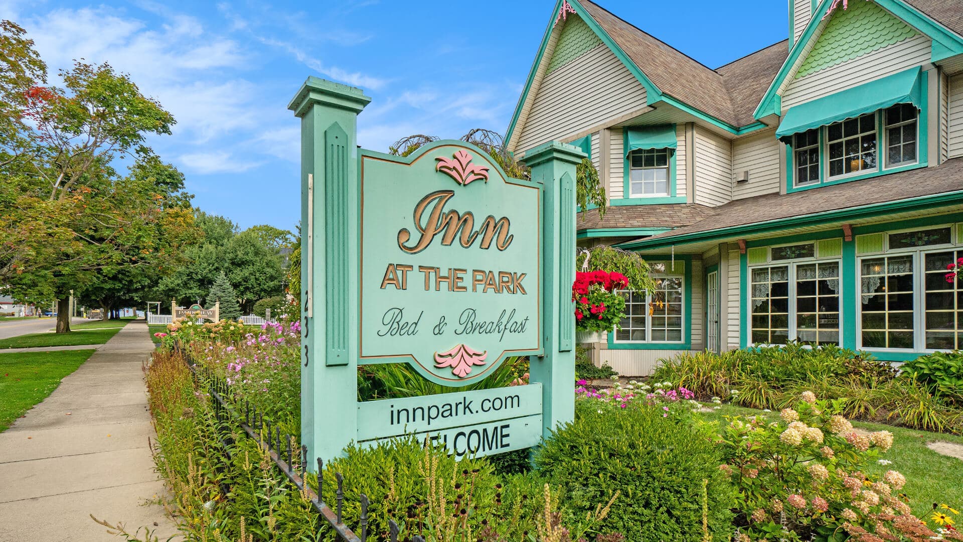 A welcoming sign for "Inn at the Park Bed & Breakfast" surrounded by colorful flowers and greenery.