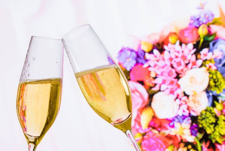 Two champagne glasses clinking together in front of a colorful floral arrangement.