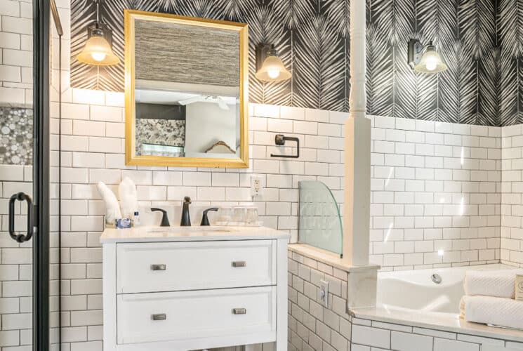 A bathroom with white tiled walls, a corner tub, and a white vanity with sink.