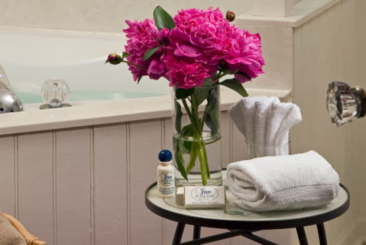 A corner soaking tub with a table of towels, flowers and bath amenities.