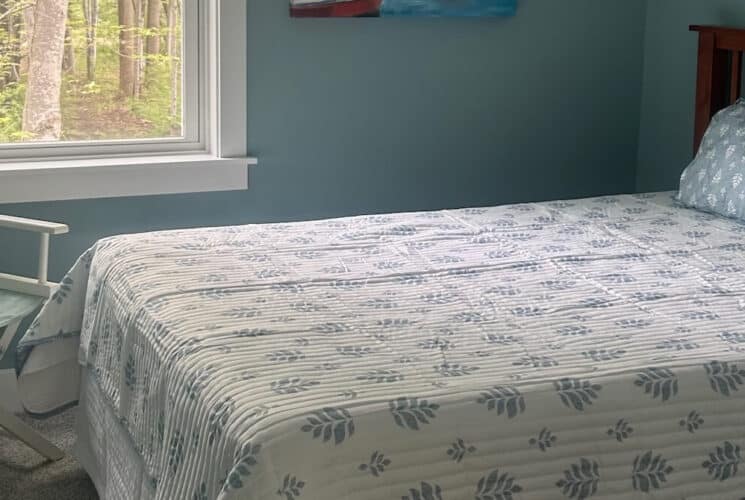 A bedroom with a bed with blue and white bedding, a wood headboard, blue walls with white trim, and a directors chair in the corner.