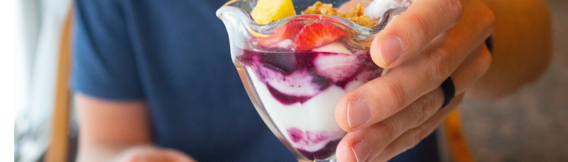 A parfait glass with yogurt, berry sauce, fresh fruit, and granola