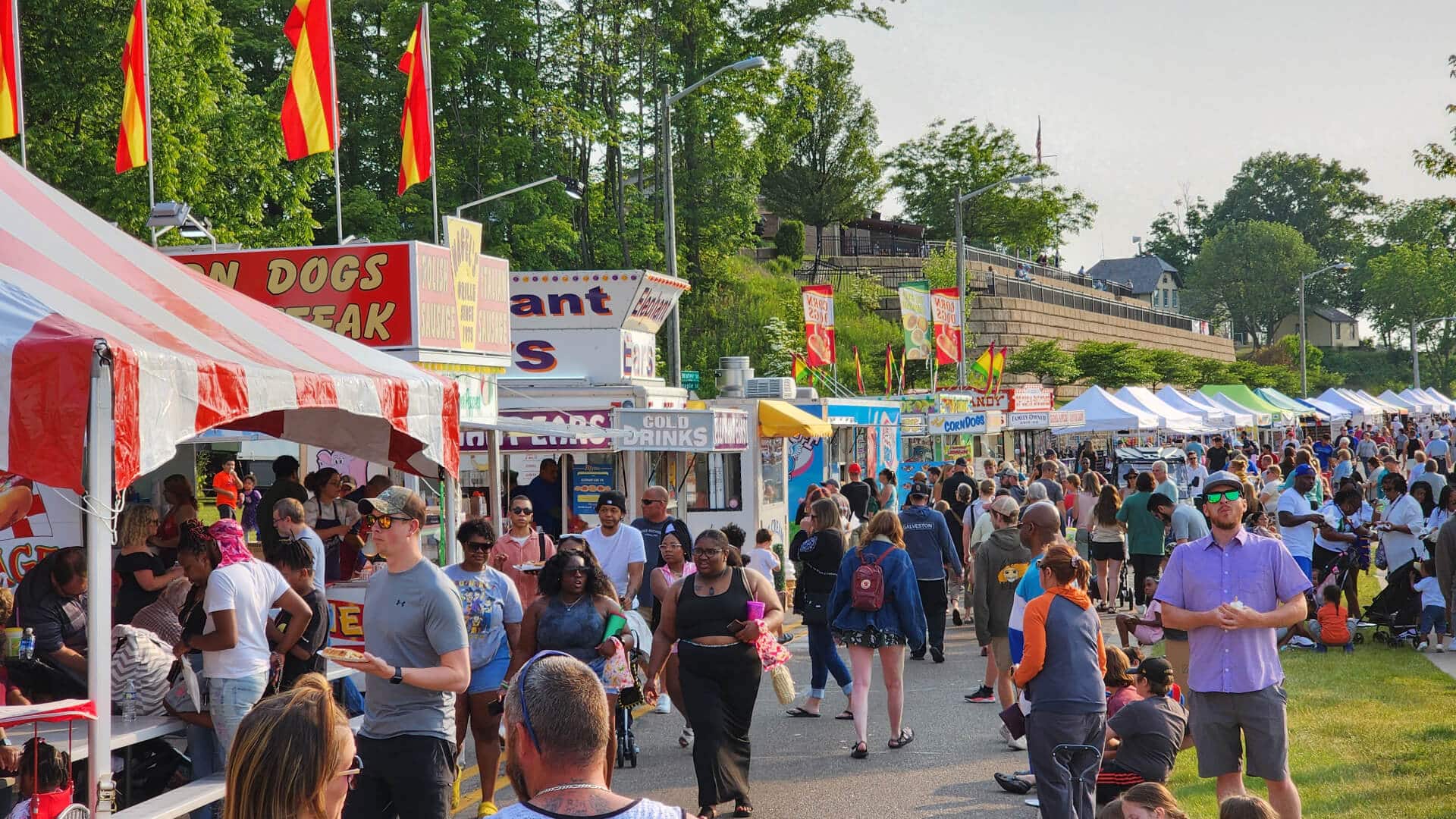 A group of people milling around the street and grass during a festival with lots of food trucks and vendors.