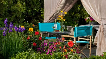 An outside sitting area with tables and chairs with wine and fresh fruit, surrounded by a garden of beautiful flowers.