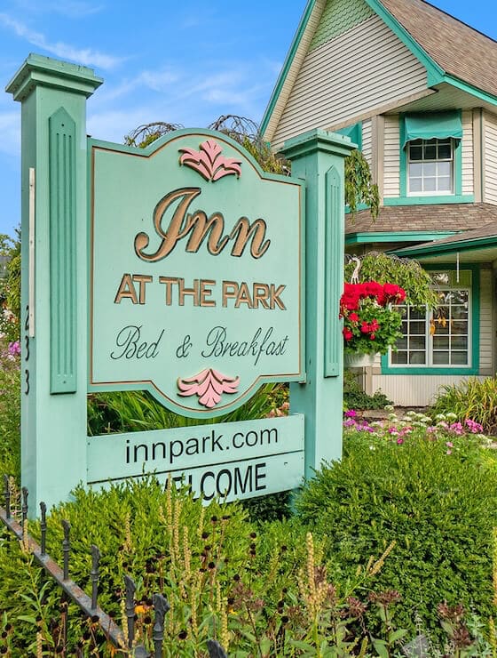 A green sign in front of a Victorian home that says Inn at the Park Bed & Breakfast