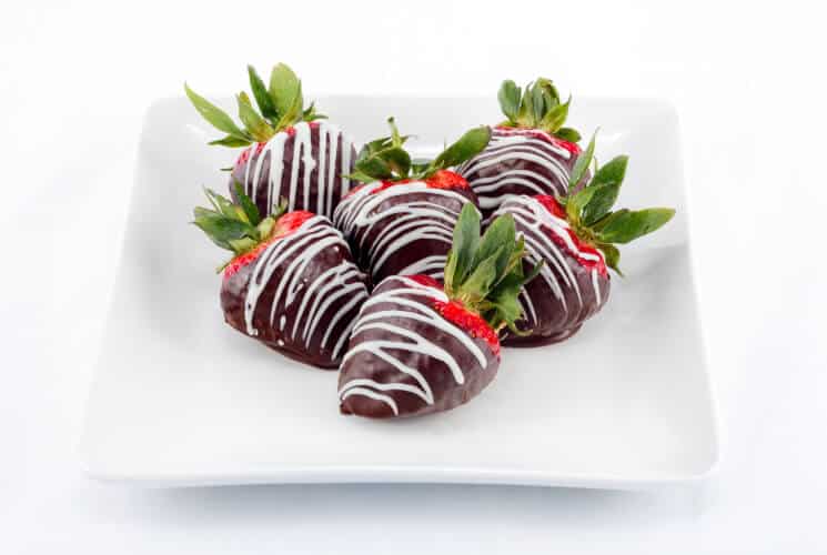 Chocolate dipped strawberries with white chocolate drizzle on a small serving plate.